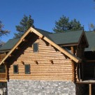 End view of handcrafted log home with full log gable end and log dormers set on stone foundation.