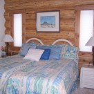 King size bed with white nightstands against handcrafted cedar log wall.