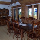 Oak dining table and chairs and classic oak china hutch in cedar log home with glass dorrs viewing out to deck with log rails.