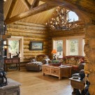 Interior great room of handcrafted log home with log truss and round top windows.