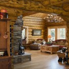 Living room of custom log home viewed through log archway. Stone fireplace and antler chandelier.