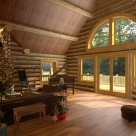 Great room of custom log home with view of forest through round top windows.