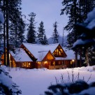 Exterior twilight photo of luxury log home in winter with multiple roof lines and transom windows.