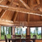 Octagonal dining room in handcrafted log home with intricate log details and log truss above dark wood dining table and chairs on area rug.