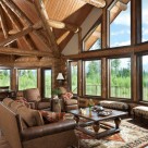 Milled log beams frame large windows with forest views in log home living room.
