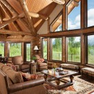 Open living room and dining room with massive glass walls surounded by log posts. Log beams and pine ceilings above in this beautiful room.