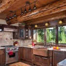 Log home kitchen with dark cabinetry, copper sink and range hood above hardwood flooring.