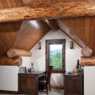 Office desk and chair tucked into gable dormer in loft of custom log home.