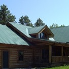 Exterior photo of handcrafted log home with metal roof, covered entry porch and small gable dormer.