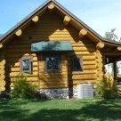 Exterior end view of Cedar log home with log purlins and covered porch.