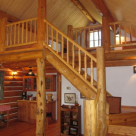 Log staircase with log railings leading to loft of small log cabin