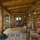 Close up photo of porch with cozy chairs on chink style log home with log rafters in ceiling.