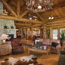 Photo of chink style log home great room with log truss, white stone fireplace, cowhide rug and antler chandelier.
