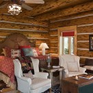 Chink style log home bedroom with cozy white chairs at foot of king size bed.