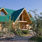 Close up photo of custom log home with green metal roof and welcoming entry way with log truss above.