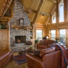 Great room of handcrafted log home with river rock chimney, leather sofa's and a full glass wall with views to the Colorado mountains.
