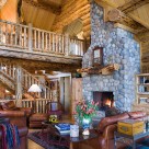 Log home greatroom with massive stone fireplace, cathedral ceilings with catwalk above sided with log railings.