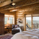 Master bedroom with custom armoire in handcrafted log home with french doors showing views to Colorado mountains from cozy queen bed.