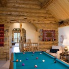Pool table in loft of custom log home with skip peeled logs, exposed beam ceiling with pine ceiling.