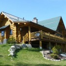 Exterior of handcrafted Cedar log home with covered porch and log railings.