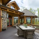 Upscale picnic table on deck of handcrafted log home with covered porch exterior stone fireplace and octagonal sunroom beyond.