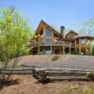 Exterior photo of luxury log home with large glass bay front, octagonal sunroom and walkout lower level.