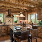 Custom kitchen cabinetry in handcrafted log home kitchen with exposed log ceiling beams and copper vent hood over range.