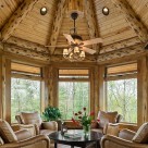 Close up photo inside log octagonal sunroom with ceiling fan over coffe table and log rafters with t&g pine for ceiling.