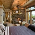 Master bedroom in custom log home with stone fireplace in corner and glass wall with view into sourthen USA forest.