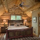 Loft bedroom with king bed backed up to full log gable with exposed log purlins above.