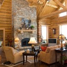 Large stone fireplace with log mantle in great room of handcrafted log home.