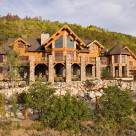 Exterior view of luxurious Steamboat Springs Colorado log home with massive stone pillars supporting full width deck and turrets on each side of home.