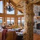 Luxury log home greatroom with stone fireplace with log mantle, massive log post and beam framing large windows with spectacular mountoin views.