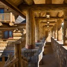Beautiful log breezway with massive stone walls supporing large log columns, header logs and roof logs with log home in background.