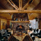 Interior great room in custom log home with log truss and stone fireplace.