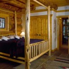 King size log bed set in master bedroom with slate floors of handcrafted log home built with massive logs.
