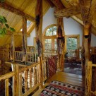 Open loft in custom log home, character logs support log purlins and log railings trim loft edge. White wall in gable with french doors leads to balcony