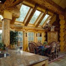 Dining room in luxury log home with slate floors set under log archway with massive logs and glass walls framed in log posts.