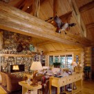 Custom log home greatroom with river rock fireplace, wicker chairs, log table and cathedral ceiling with exposed log beams.