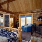 Master bedroom in Colrado log home with wood stove near a log bed and views through french doors.