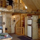 Interior of log home with spiral staicase leading to open loft beside antique looking refrigerator.