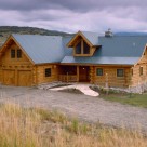 Exterior view of entry side of custom log home with metal roof and 2 car attached garage.