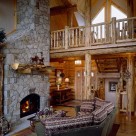 Log home greatroom with sectional couch facing large stone fireplace, Cathedral ceilings with open loft supported by log post and beams and log raings along the edge of loft.