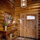 Interior view of arch top wood door with sidelite panel in handcrafted log home with pendant light and custom wood bench to side.