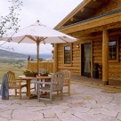 Flagstone patio with round wood table and white umbrella in front of handcrafted log cabin.
