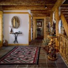 Foyer of log home with slate floors, oriental rug and Indian bronzes set on burlwood stands.