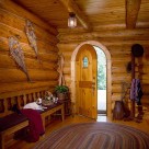 Inteior image of round top wood entry door in foyer of handcrafted log home with oval area rug, red bench and snowshoes mounted on log wall.