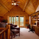 Home office in loft of handcrafted log home with sliding glass doors in log gable leading to balcony with log railings.