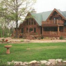 Exterior photo of custom log home with green metal roof with sveral gables and balcony with log railings.