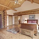Master bedroomwith cathedral ceilings in handcrafted log home with victorian style bed, hardwood floors and white accent wall framed in log beams.